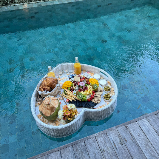 a charcuterie cheese platter served on a floating basket on a pool with pastry orange juice and coconut by Grazie Bali
