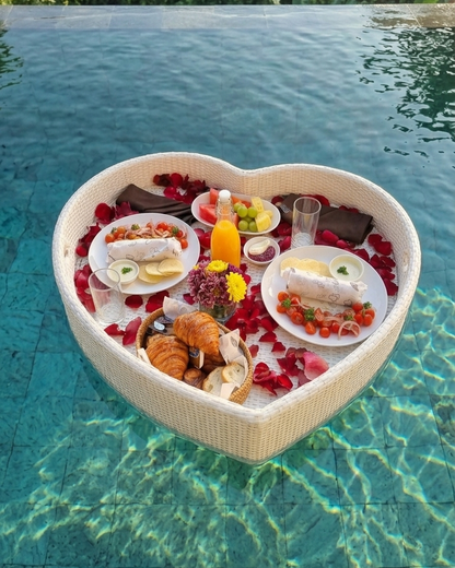 Heart-shaped dining setup with food on a pool float surrounded by lush greenery