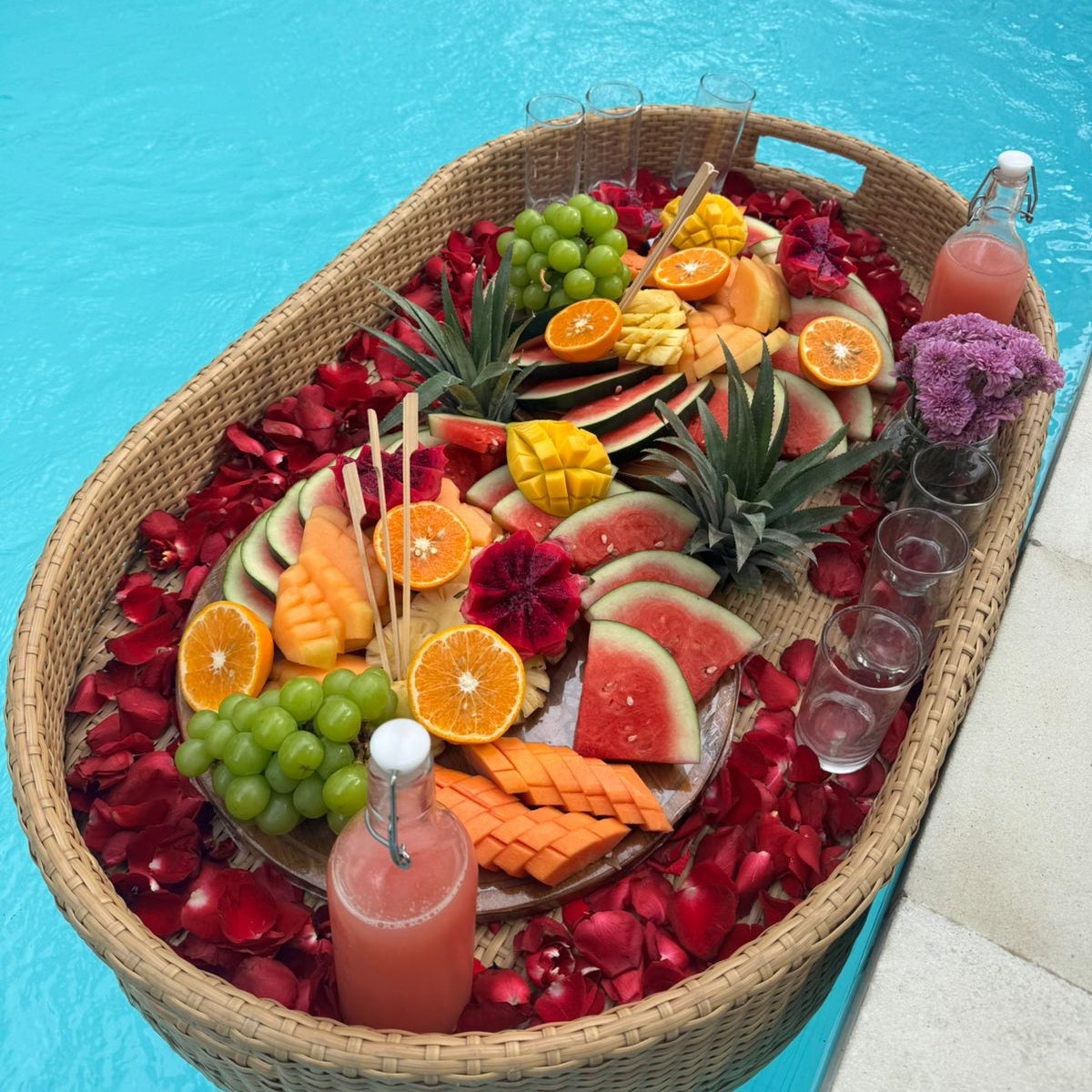 Fruit platter with drinks on a woven tray by a pool