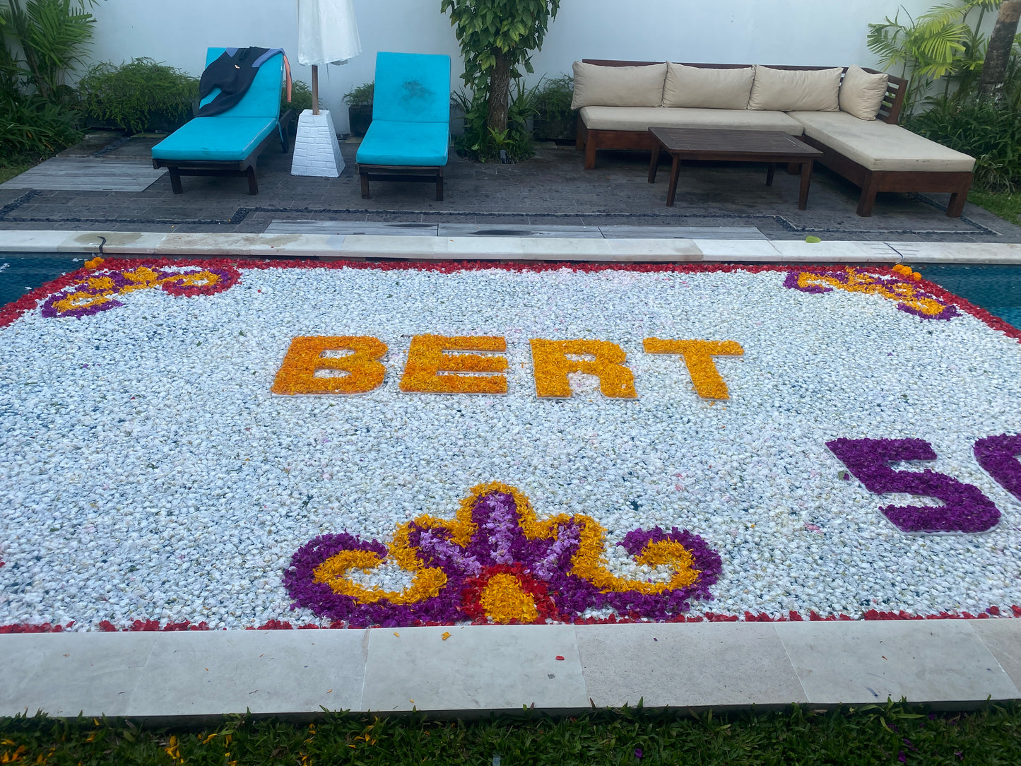 a pool villa in uluwatu bali decorated with white flowers petals and decorated with yellow and purple flowers for 50th birthday